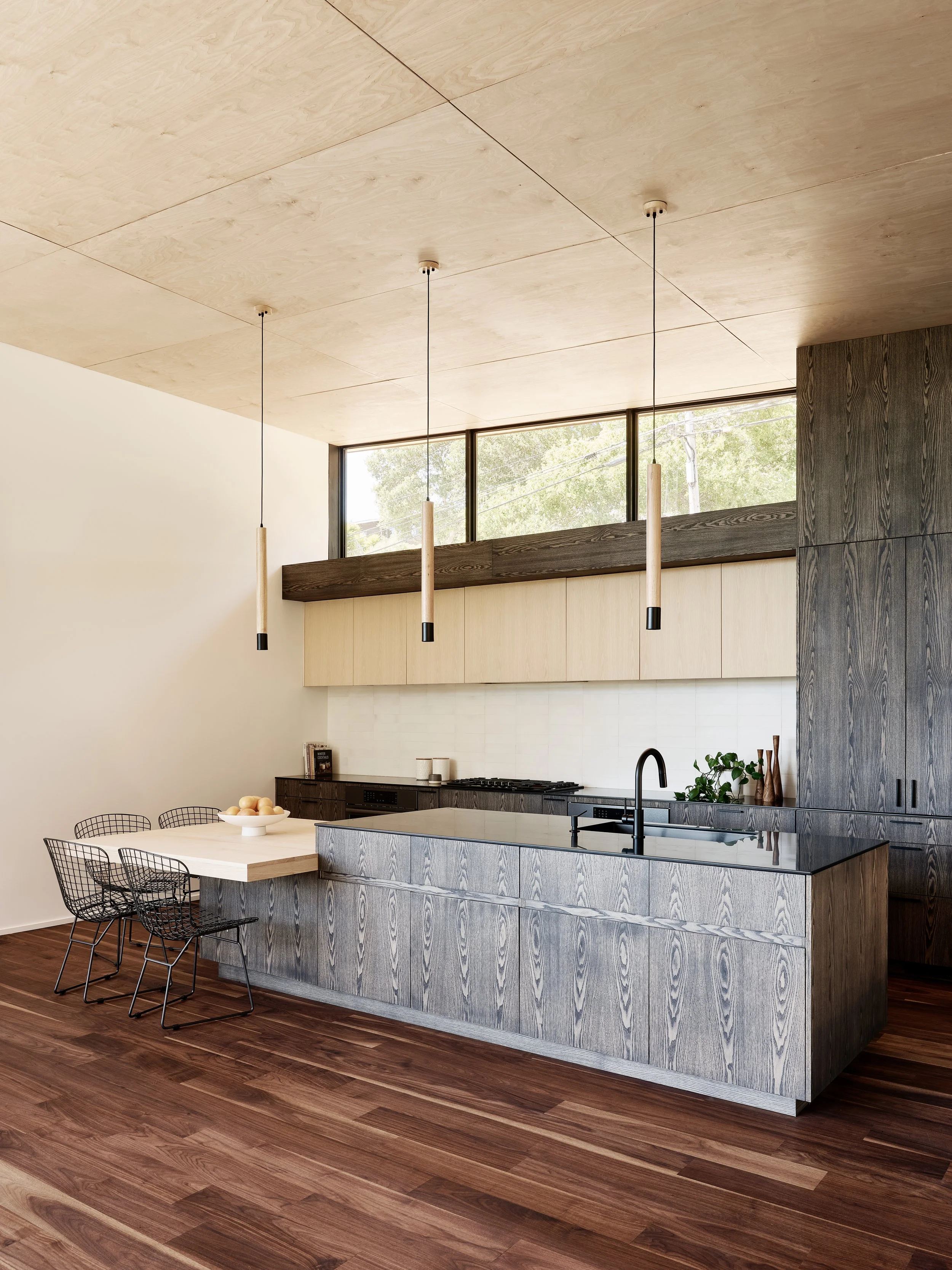Modern kitchen with a large wooden island, black faucet, and pendant lights hanging from the ceiling, with a wooden floor and cabinets.