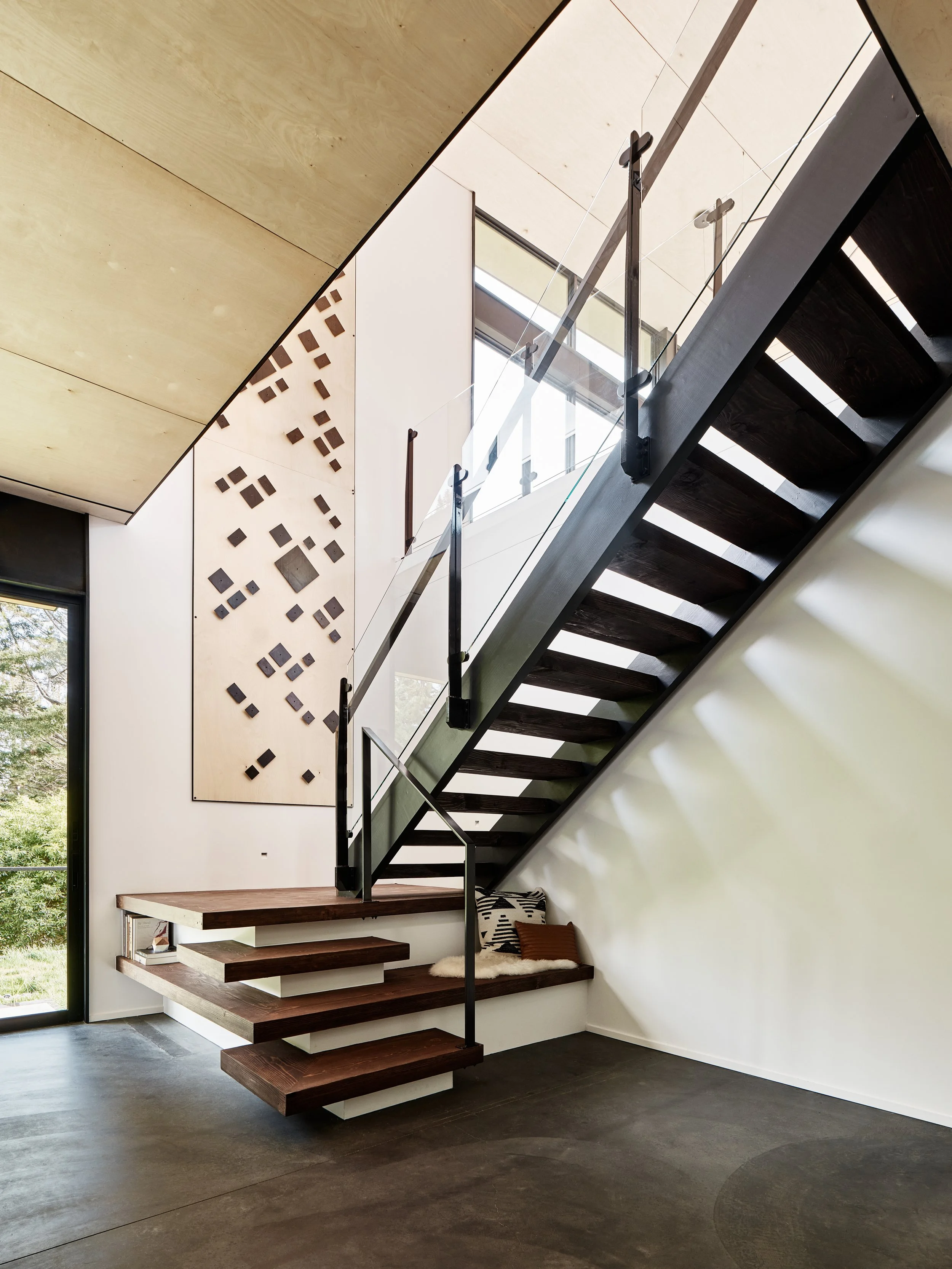 Modern interior staircase with dark wooden steps, glass and metal railing, and a wall with geometric wood and metal wall art.
