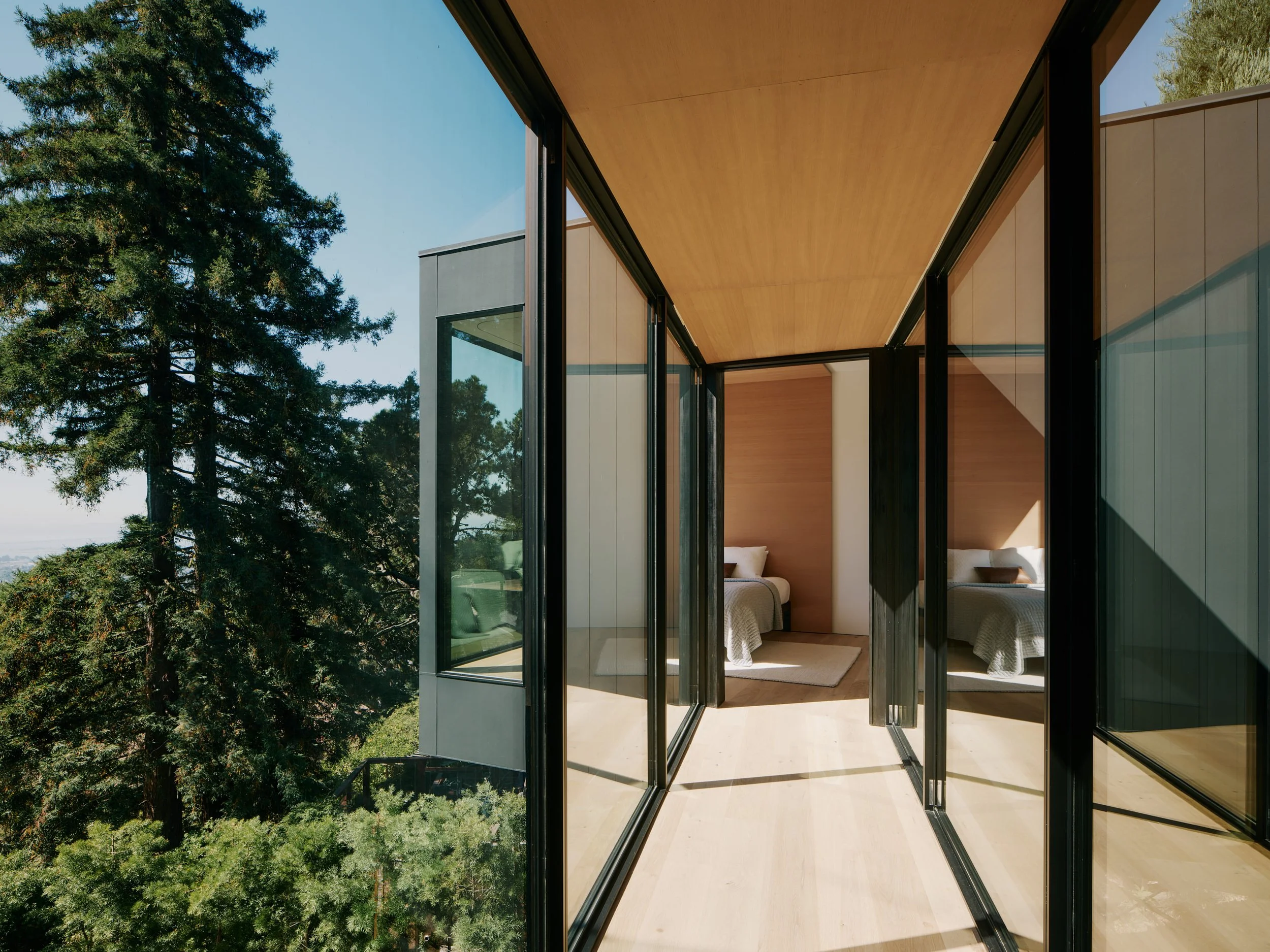 Modern house with large glass windows opens to a balcony with trees in the background.