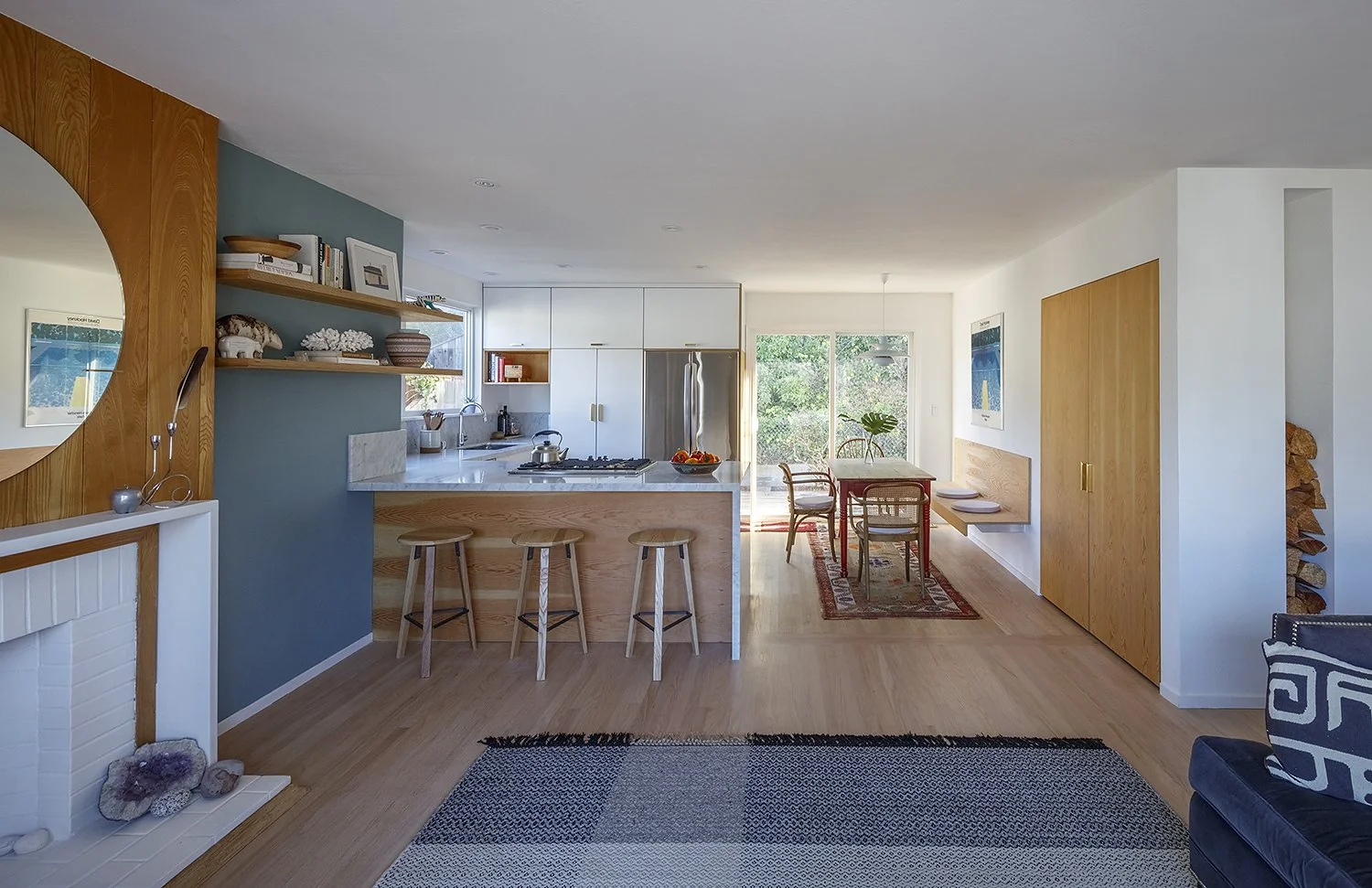 Open-concept kitchen and dining area with modern design, wooden accents, white cabinets, and large windows with views of greenery.