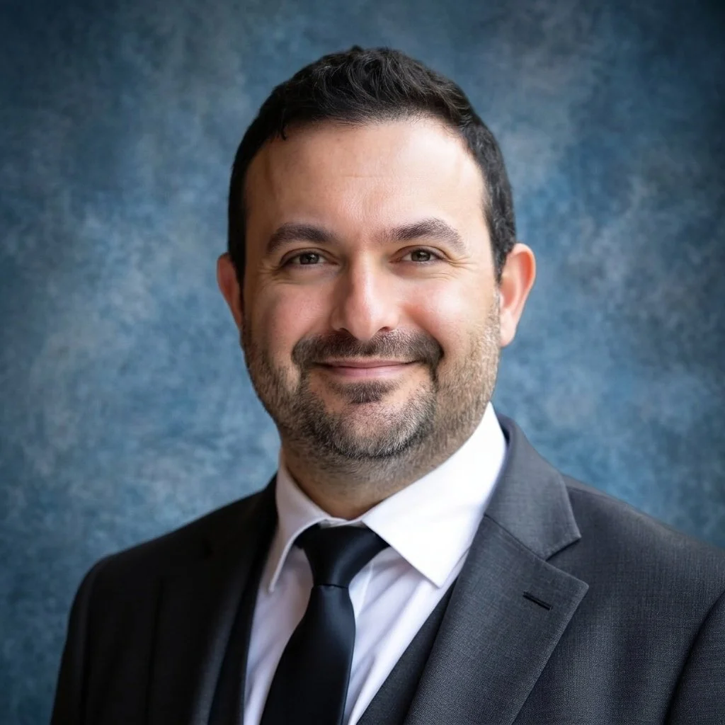 A man in a suit smiling against a blue background.