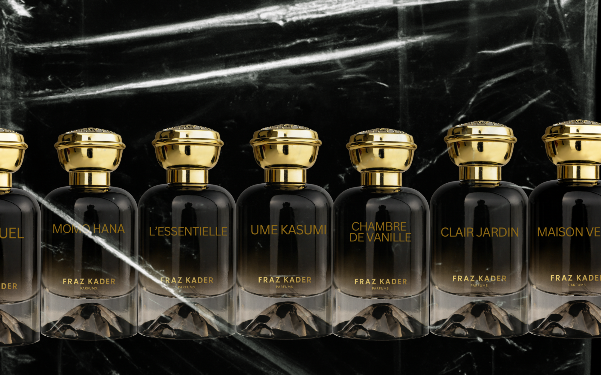 Six black perfume bottles with gold caps, labeled with gold text, lined up on a black marble surface with a black marble background.