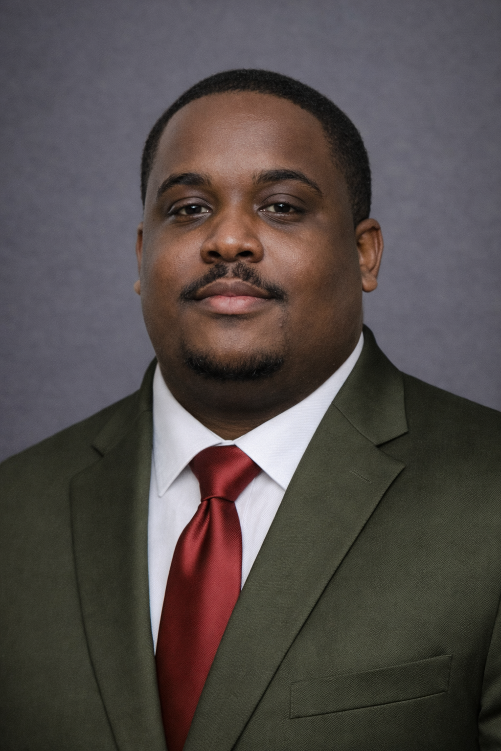 Portrait of a man in a dark green suit, white shirt, and red tie, against a dark grey background.