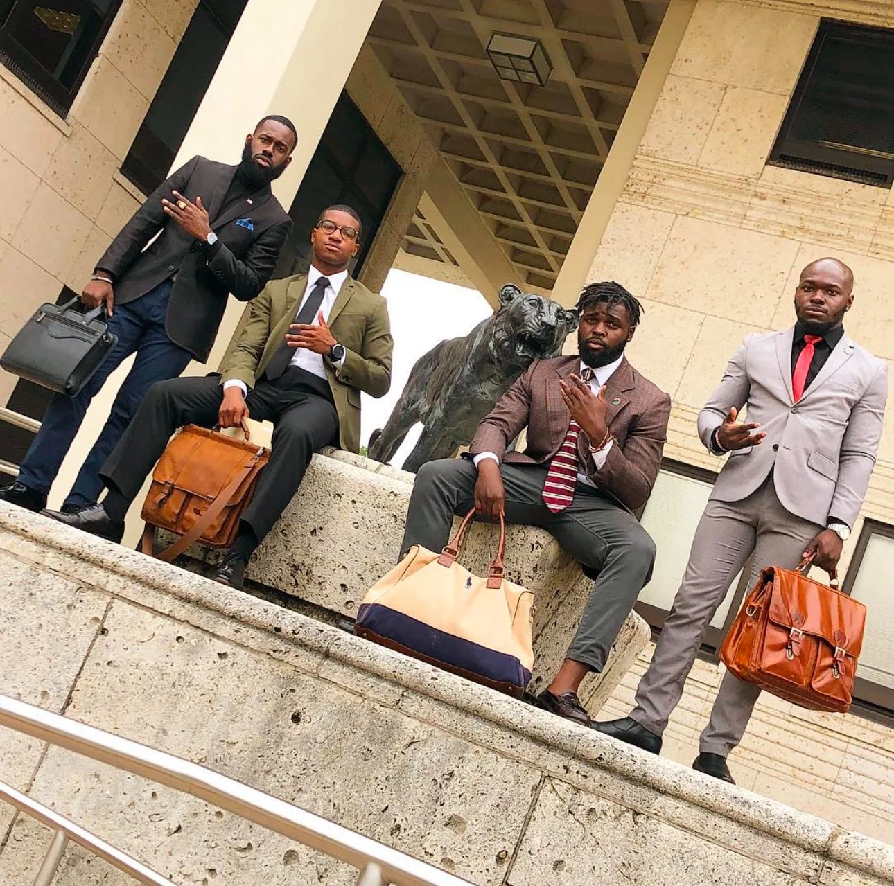 Five men dressed in suits with briefcases, posing on a ledge near a lion sculpture in front of a government or institutional building.