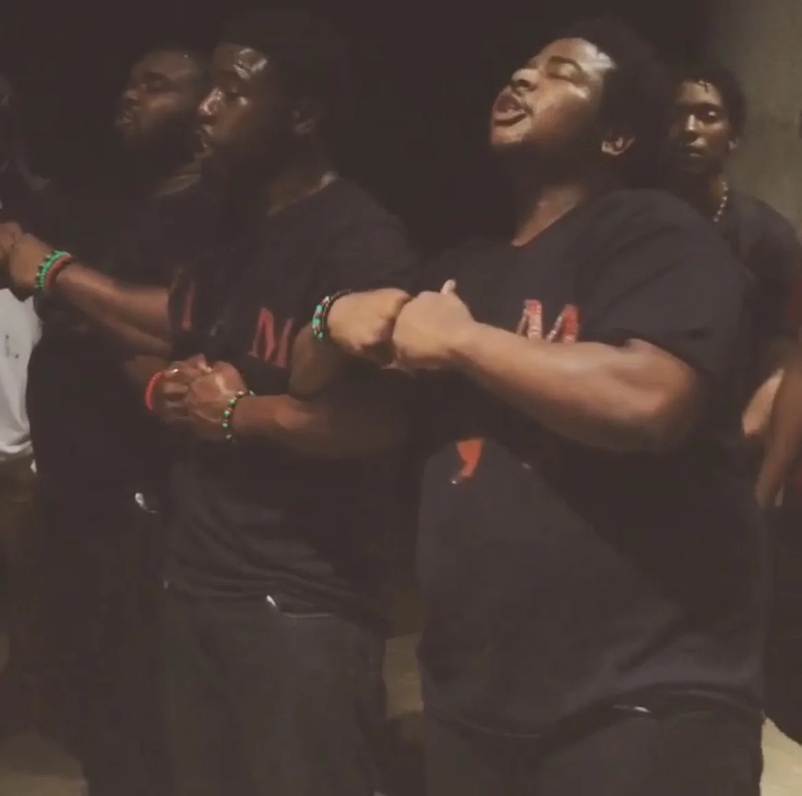 Group of people holding hands in a circle, smiling, and enjoying themselves, wearing black clothing and colorful bracelets.