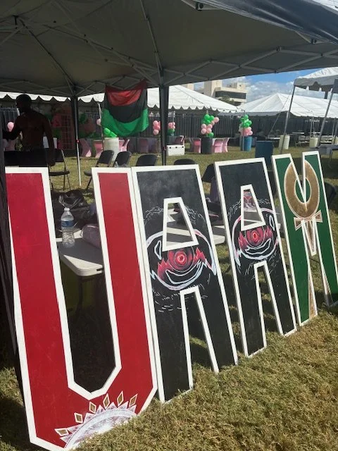 Large decorated UADA signs at an outdoor event under tents, with balloons and tables in the background.