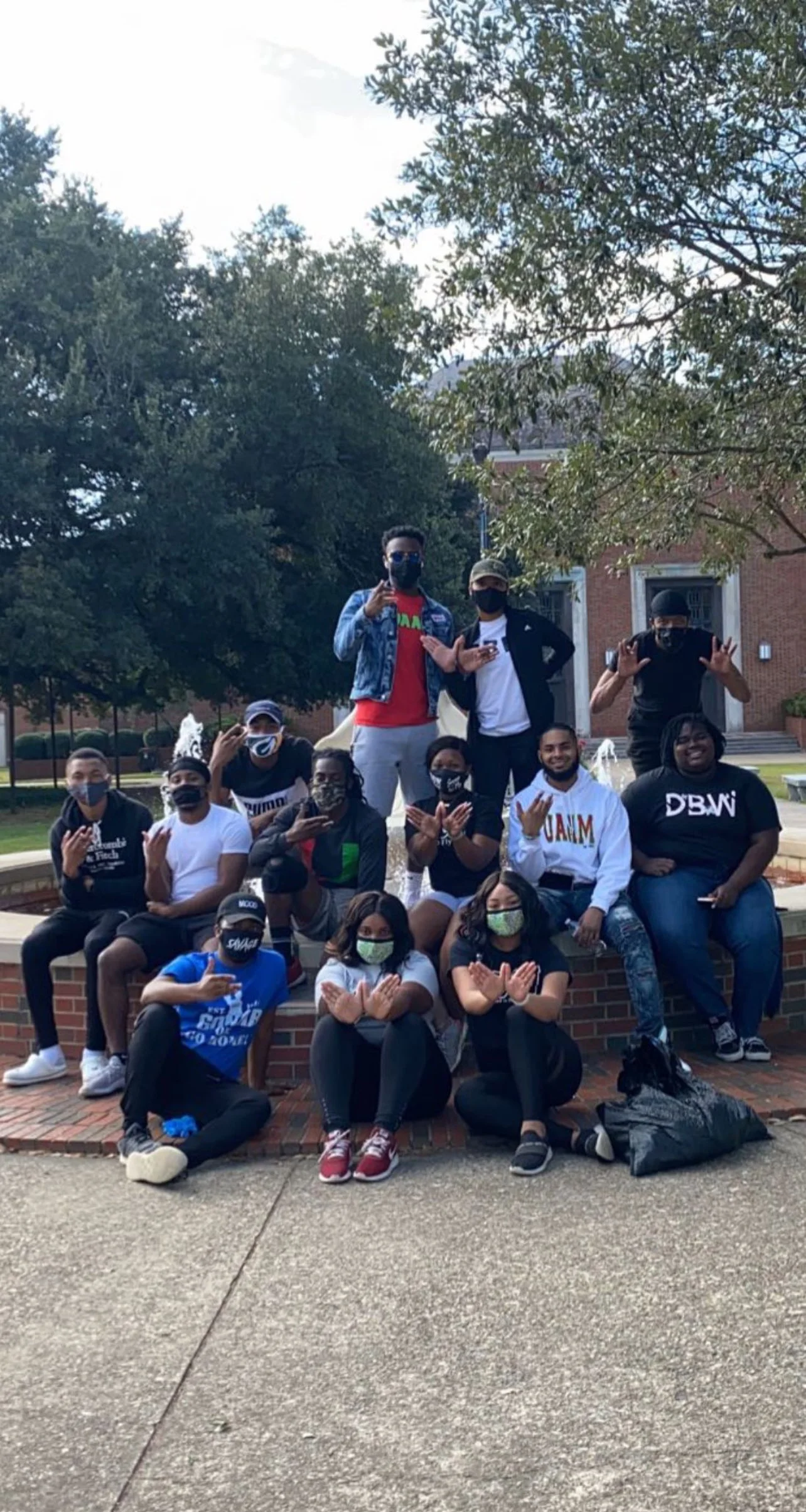 A group of people wearing masks posing in front of a brick building and a fountain.