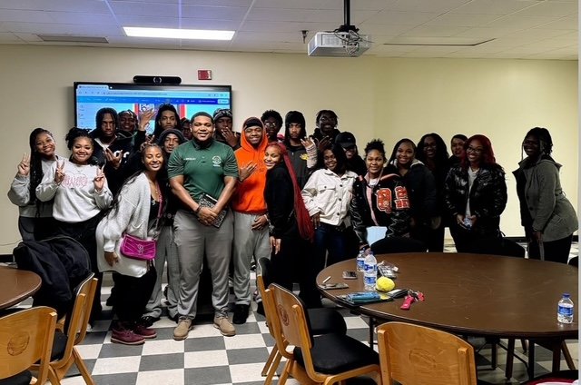 Group of students and a teacher in a classroom, standing together for a photo.