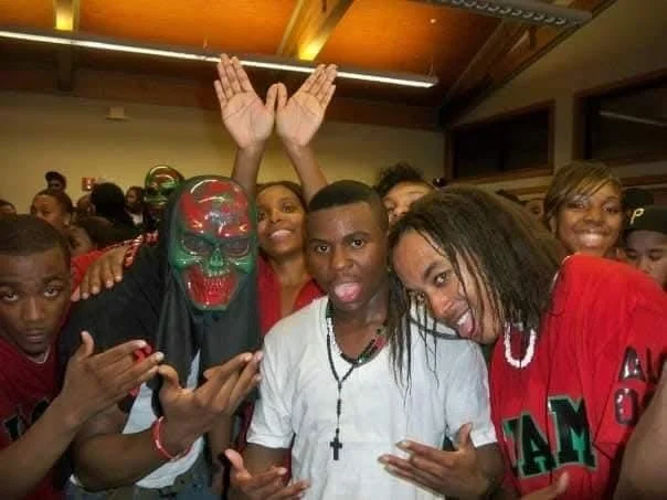 Group of young people at a party, some making gestures and smiling, with one person wearing a colorful skull mask.