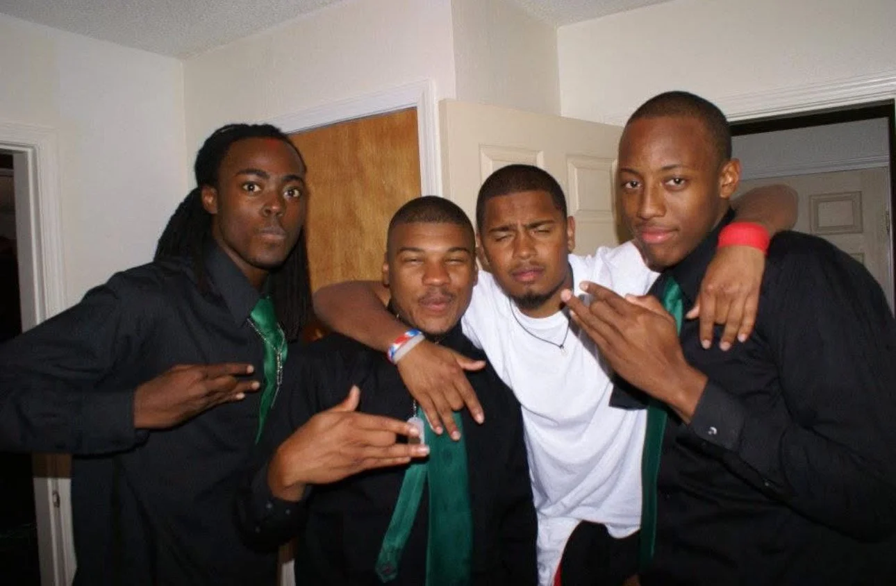 Four young men standing together indoors, posing for a photo.