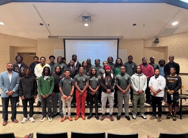 Group photo of young men and women standing on a stage in a conference room, with a projector screen in the background displaying 'Closing Remarks'.