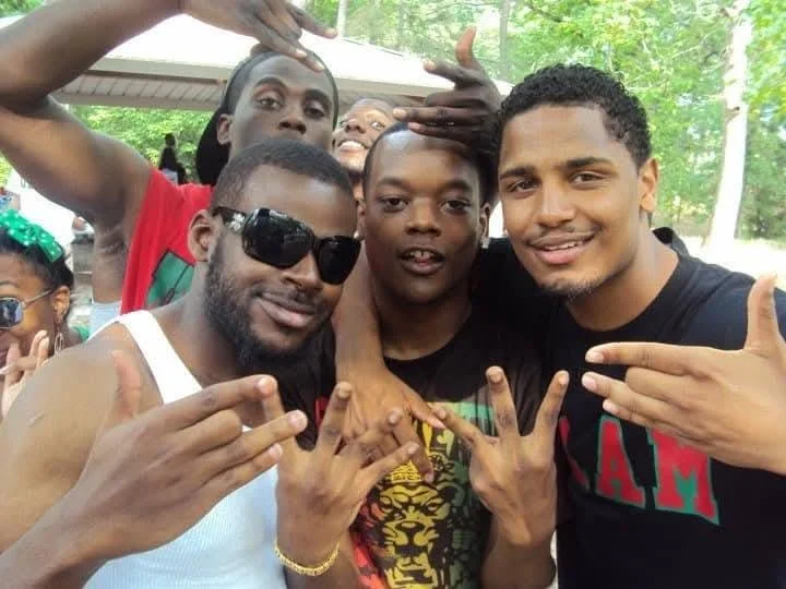 Group of young men and kids at an outdoor gathering, making hand gestures and smiling.