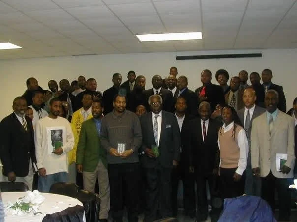Group of people gathered in a conference room, some holding books or awards, dressed in formal and semi-formal attire, posing for a photo.