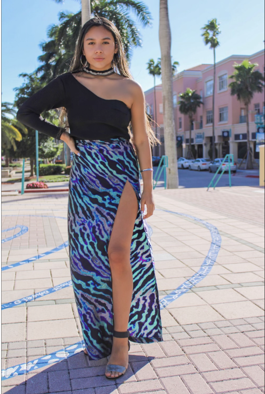 AZUL SAFARI — A bold statement set with a sculpted one-sleeve top featuring a cutout neckline, sweetheart shaping, and sparkling trim. Finished in purple zebra print, the skirt’s dramatic slit balances the silhouette for a curve-enhancing look.