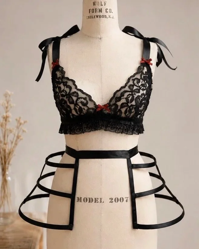 REBEL ROMANCE BRALETTE & CAGE — A  bralette detailed with red bow accents and bow-tie straps with a statement cage pannier petticoat. Built with spiral steel boning, the silhouette creates an avant-garde contrast.