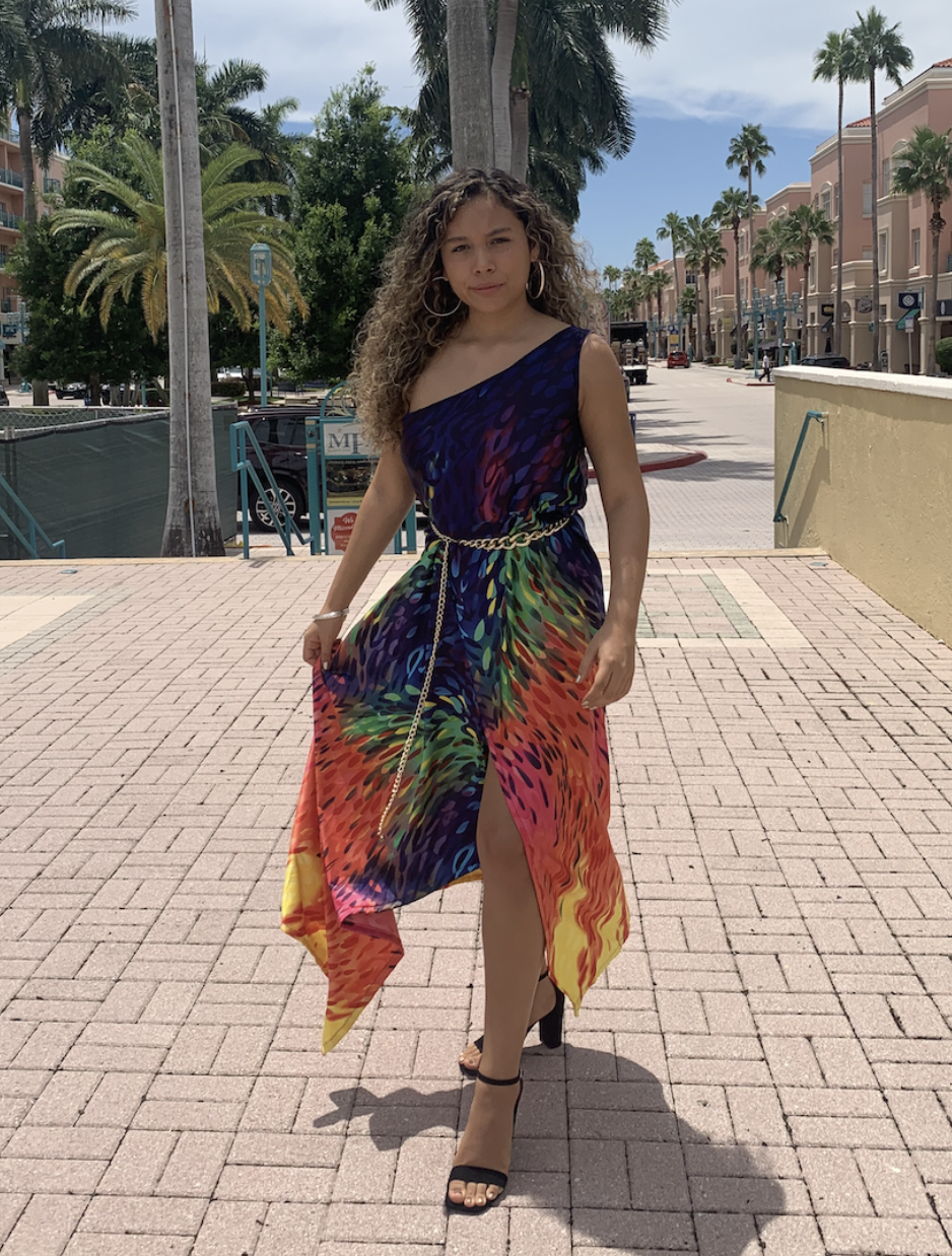 MYKONOS MADNESS — A vibrant one-shoulder dress featuring a flowing panel skirt and asymmetrical bodice. Finished with a gold chain belt and front slit, it captures effortless Mediterranean glamour and a carefree summer spirit.