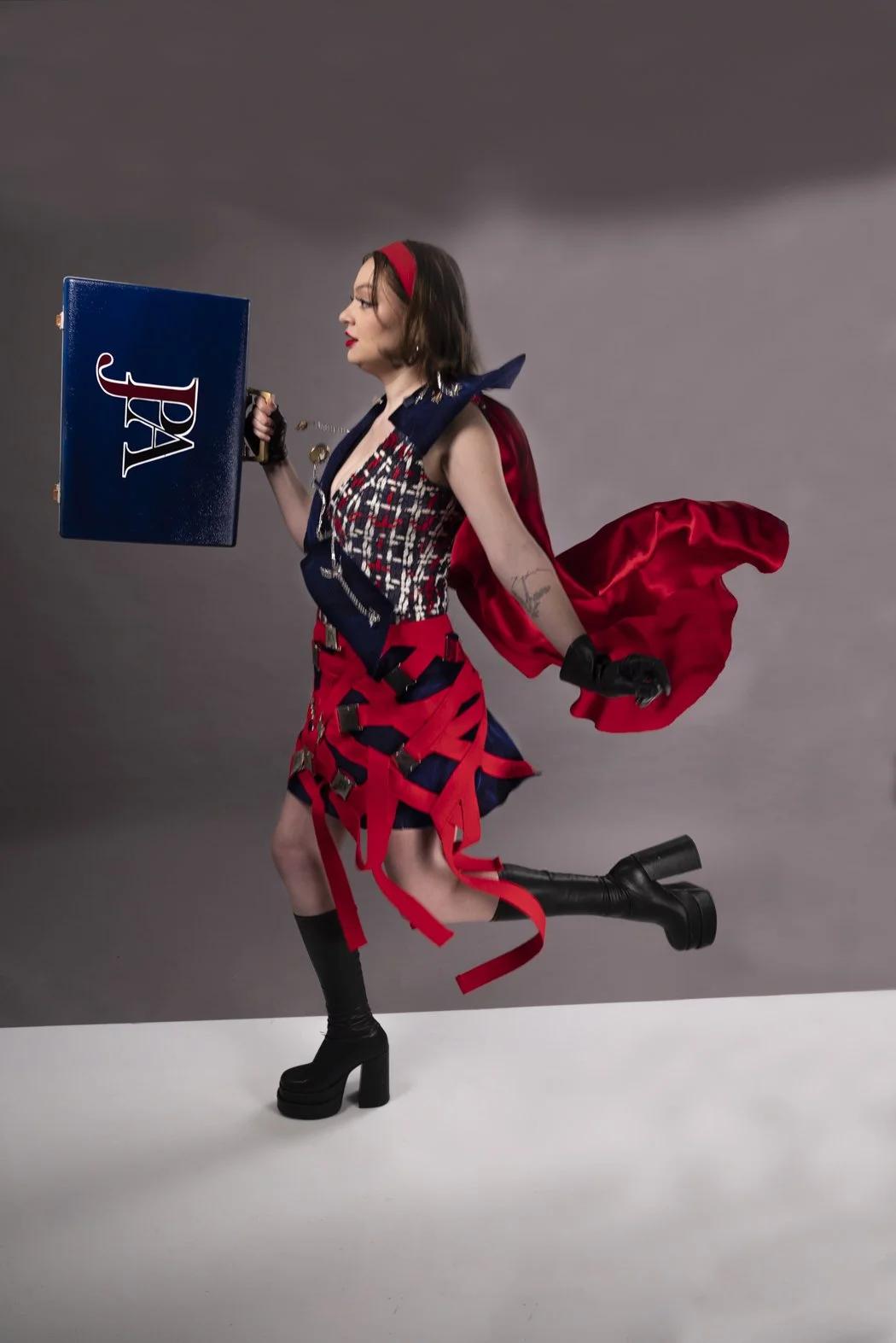 EN ROUTE: LOOK 2 – A sculptural asymmetrical seatbelt skirt dress in boucle with a navy velvet lapel and layered statement detailing. Finished with reworked vintage-inspired travel accents for a conceptual couture silhouette.
