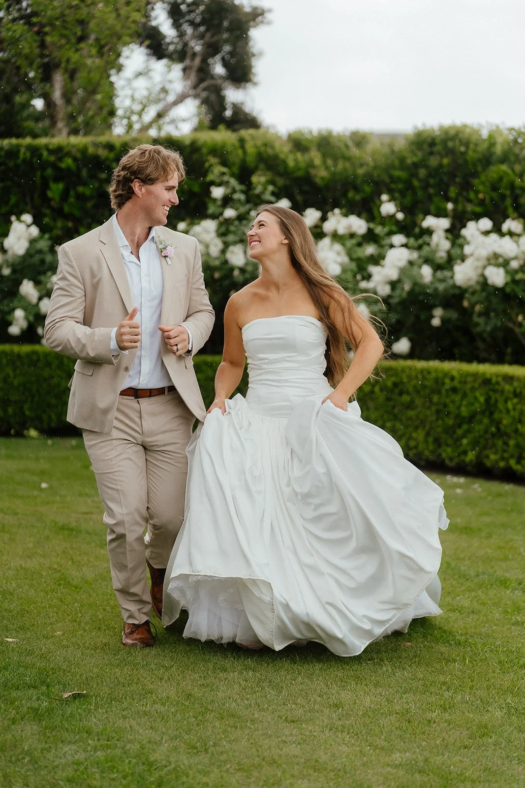 A bride and groom smiling at each other at an outdoor wedding, with greenery and white flowers in the background at Twin Oaks Golf Course Wedding Venue.