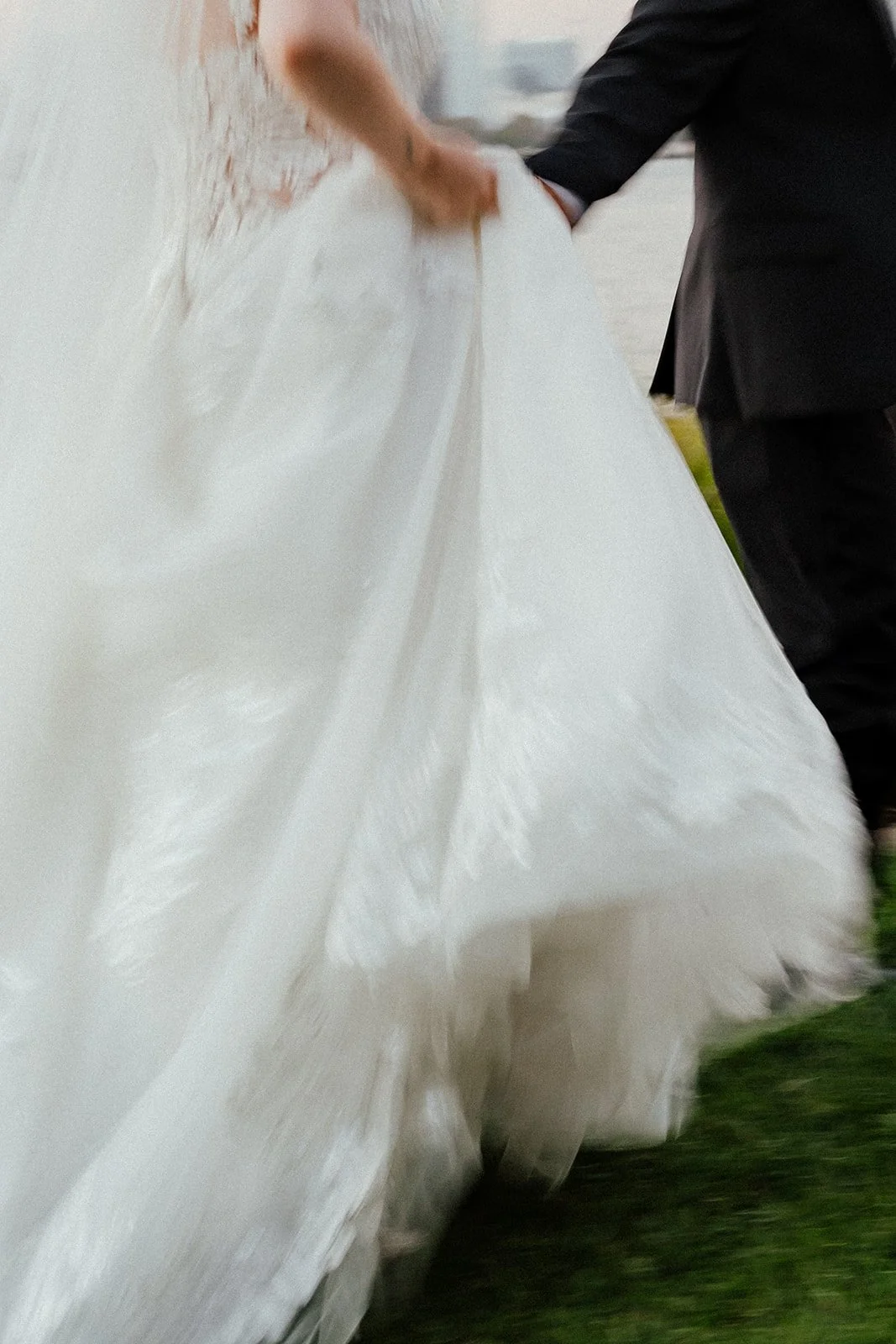 Close-up of a bride in a white wedding dress and a groom in a black tuxedo, holding hands during their wedding dance during Coronado Elopement.