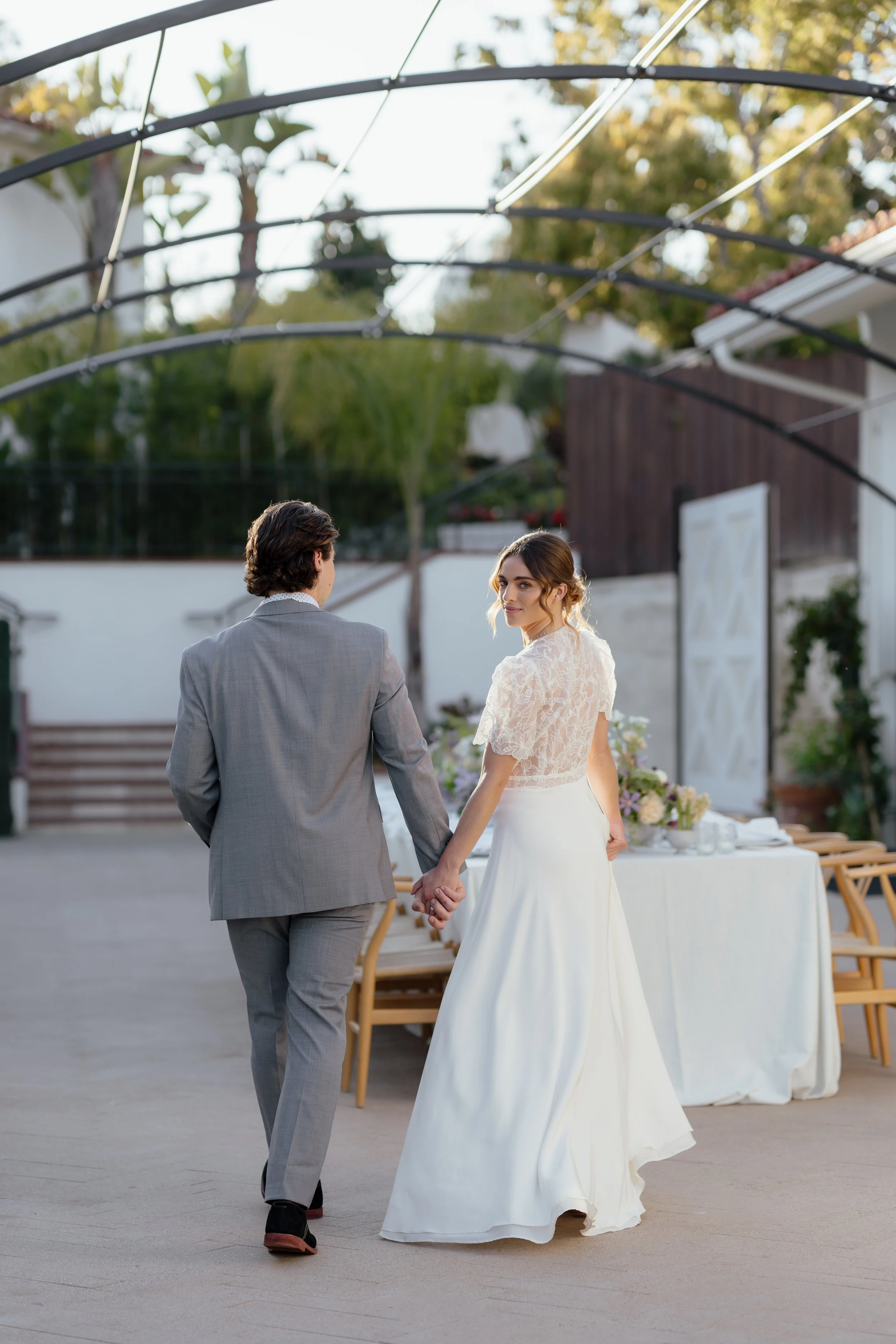 Bride and groom holding hands and walking at their wedding reception outdoors in the late afternoon.