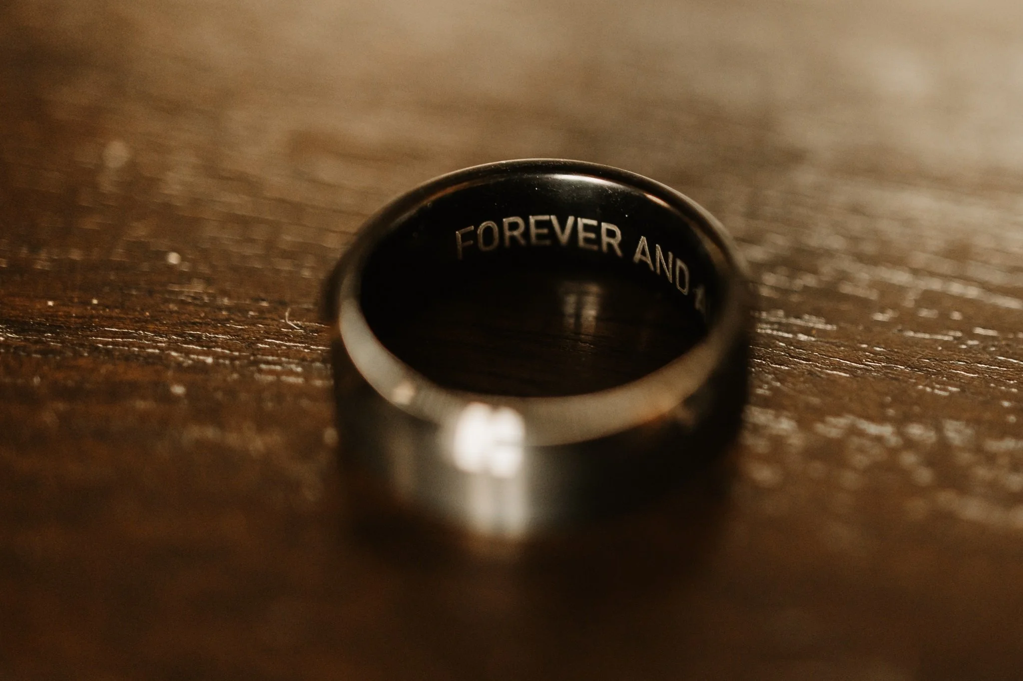 Close-up of a silver ring engraved with the phrase 'FOREVER AND' resting on a wooden surface.