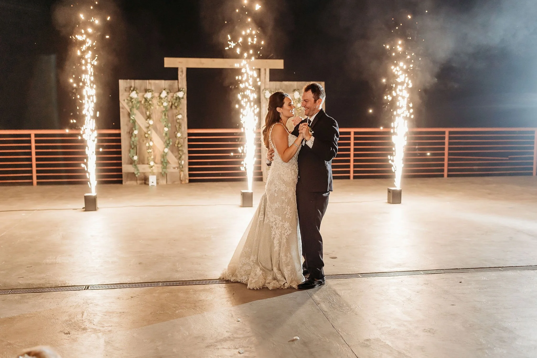 A bride and groom dancing at their wedding reception, surrounded by fireworks and sparklers in the background.