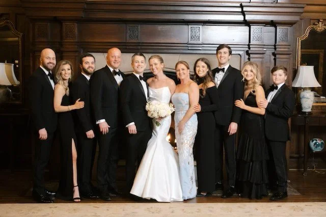 Group of people dressed in formal attire, celebrating a wedding in a room with wooden paneling and vintage decor.