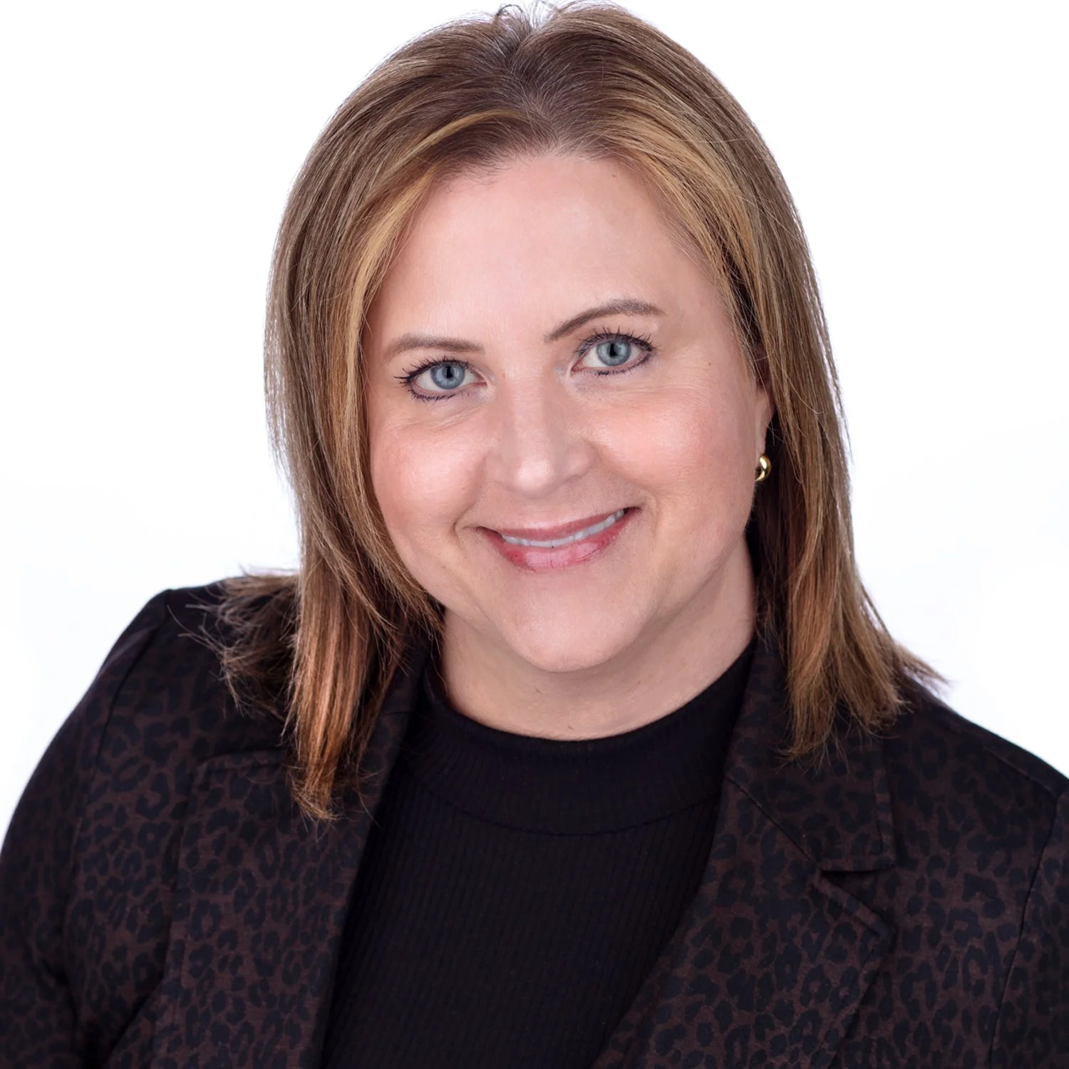 Headshot of a woman with shoulder-length light brown hair, blue eyes, and a friendly smile, wearing a dark patterned blazer over a black top.