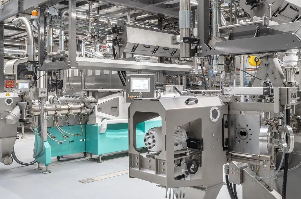 A complex industrial machine with various pipes, valves, and control panels in a factory setting.