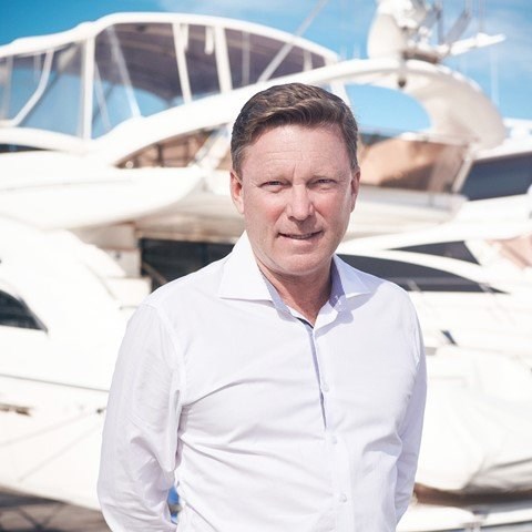 A man in a white shirt standing in front of docked yachts