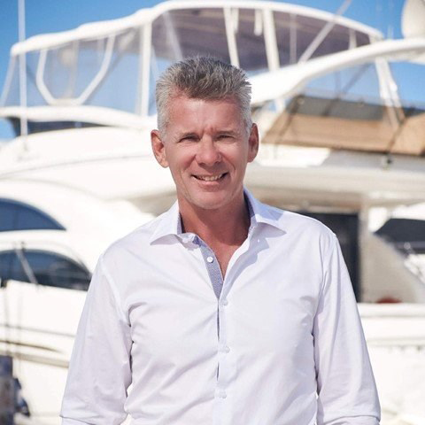 Man in white shirt smiling in front of docked boats