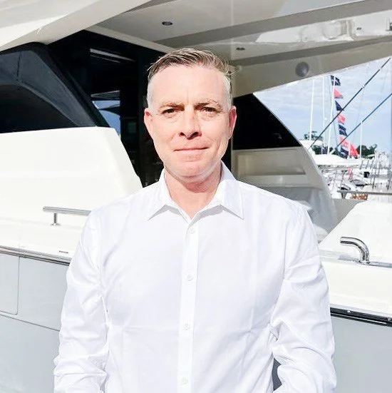 Man wearing a white dress shirt standing in front of a yacht.