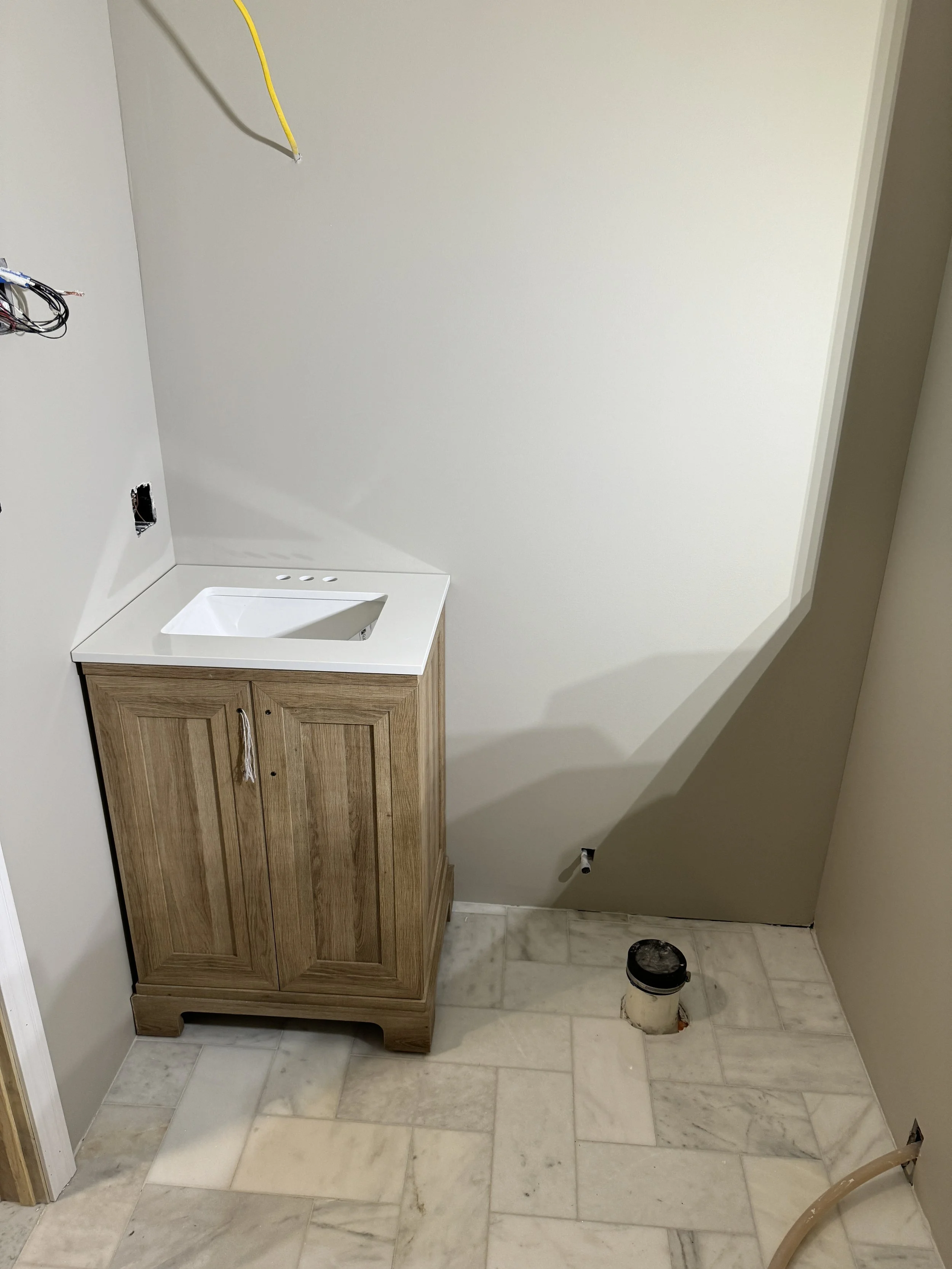 Bathroom under renovation with a small wooden cabinet with a sink, unfinished plumbing, and exposed electrical wires.
