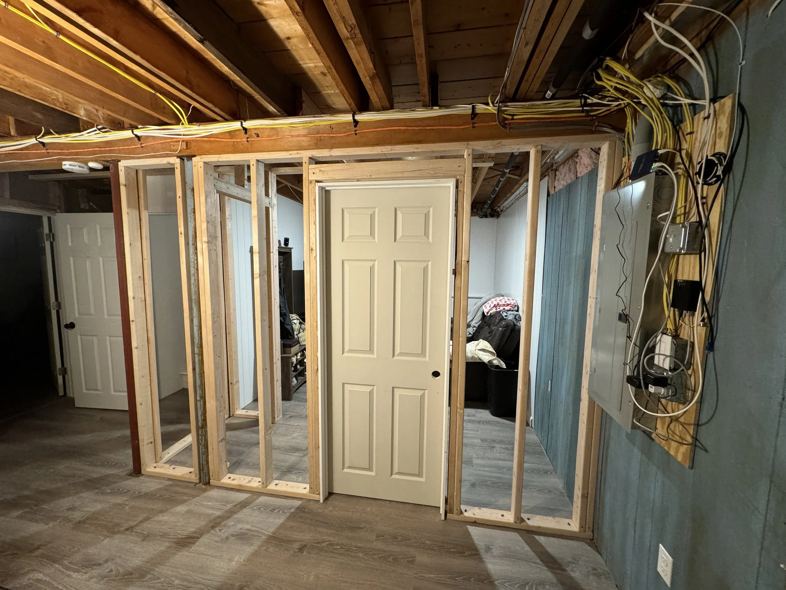 Room under construction with exposed wooden framing, a closed white door, and electrical wiring on the wall.