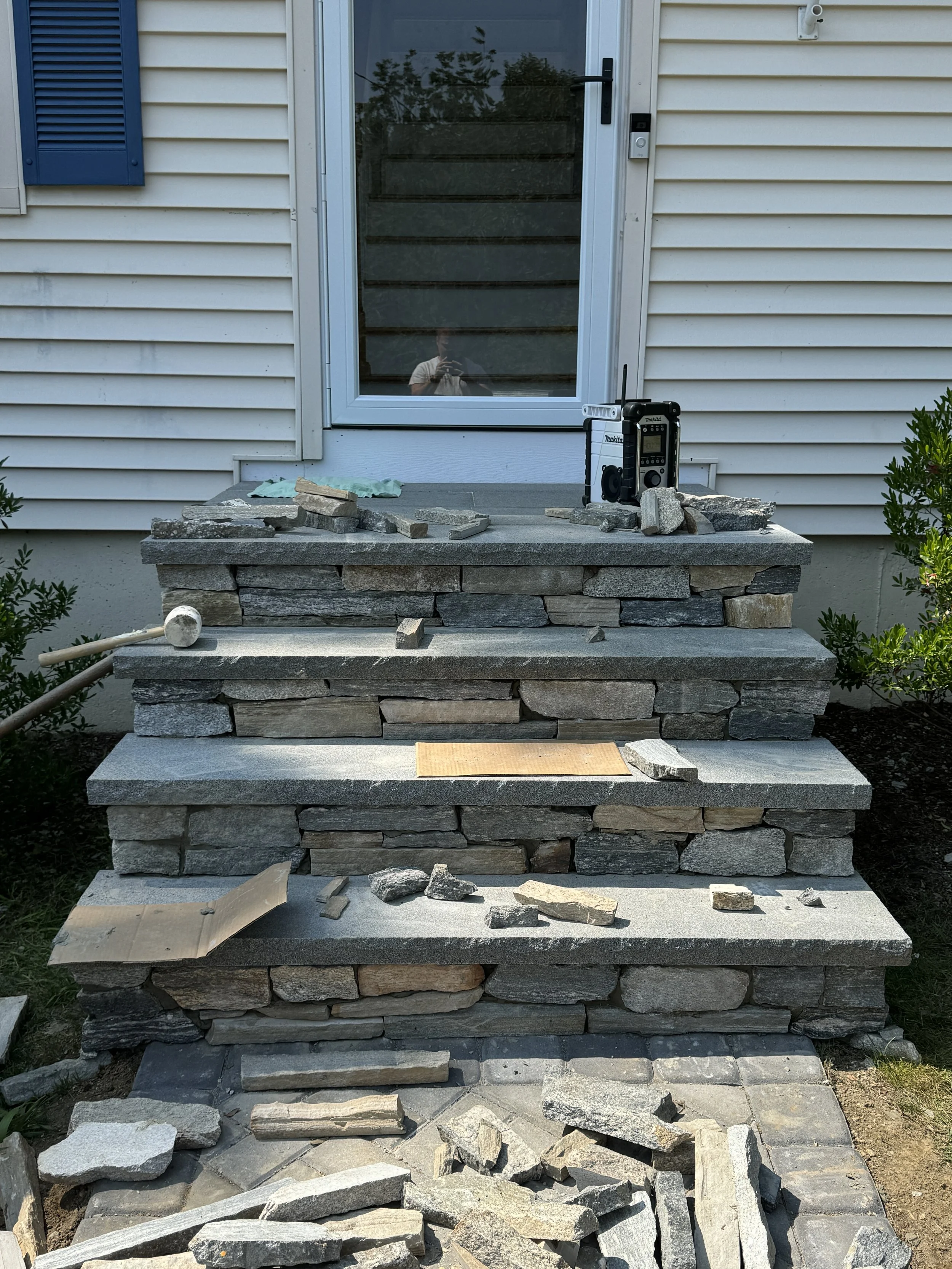 Stone steps under construction leading to a house door, with construction tools and materials on the steps and ground.