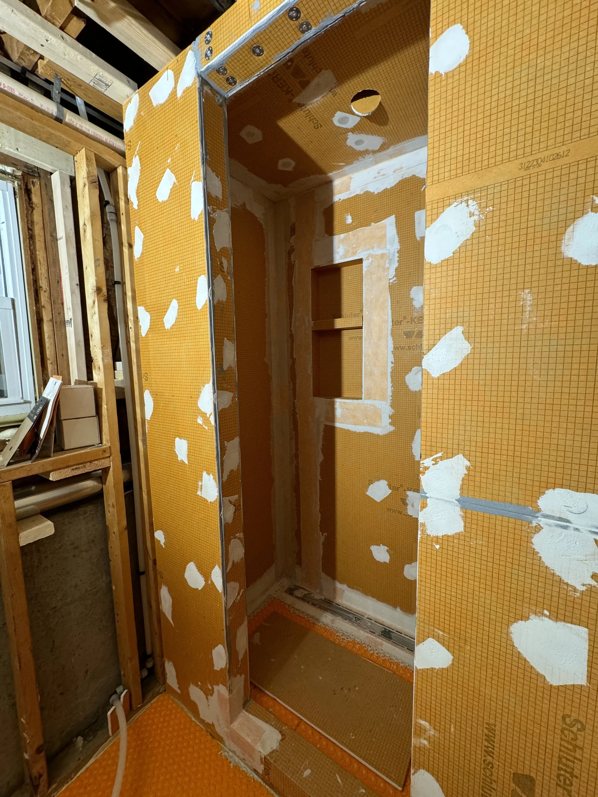 Construction of an elevator shaft with yellow insulation panels and drywall patches in a building under renovation.