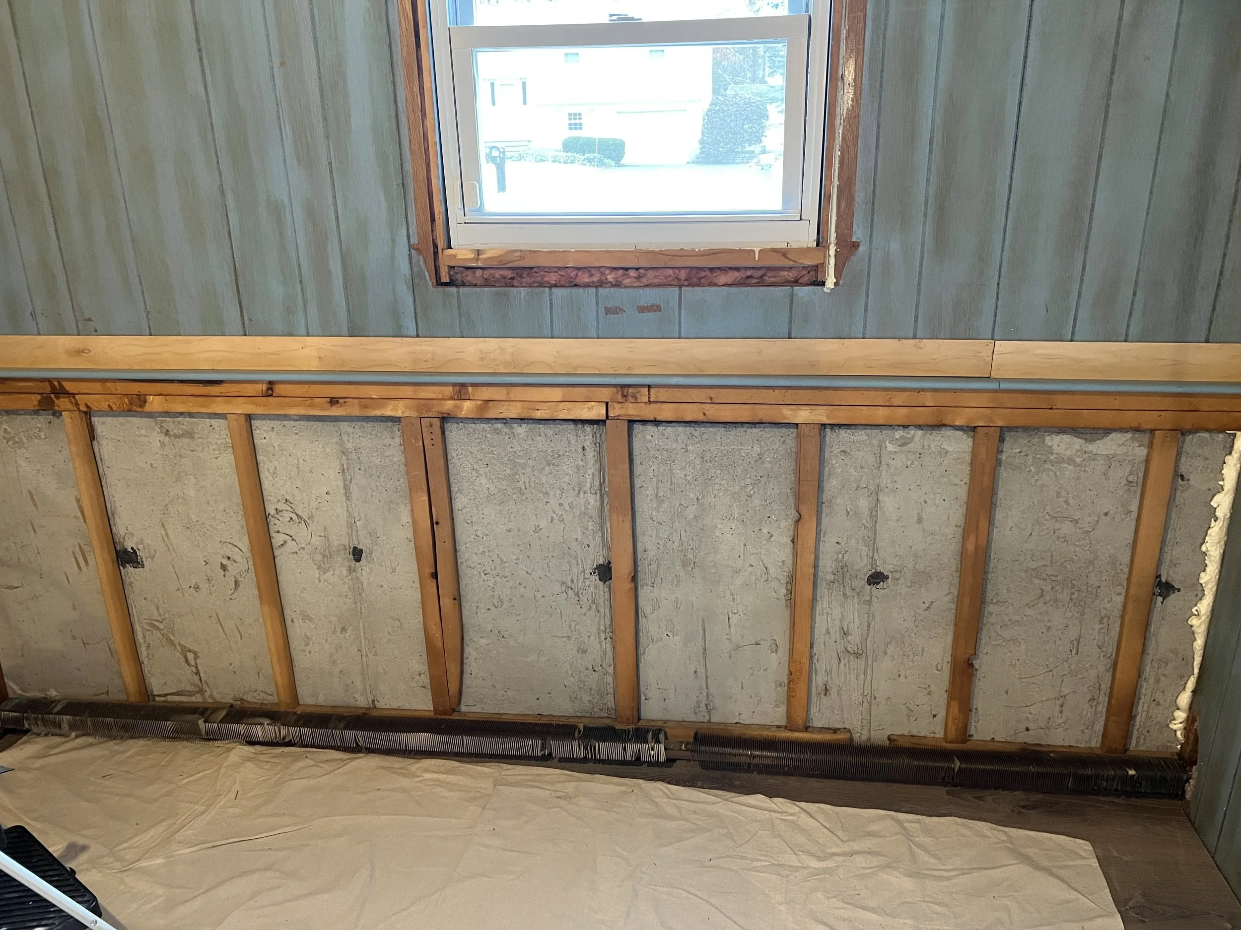 Interior wall remodeling in progress with exposed wall studs, insulation, and a partially installed window with visible surrounding rough framing.