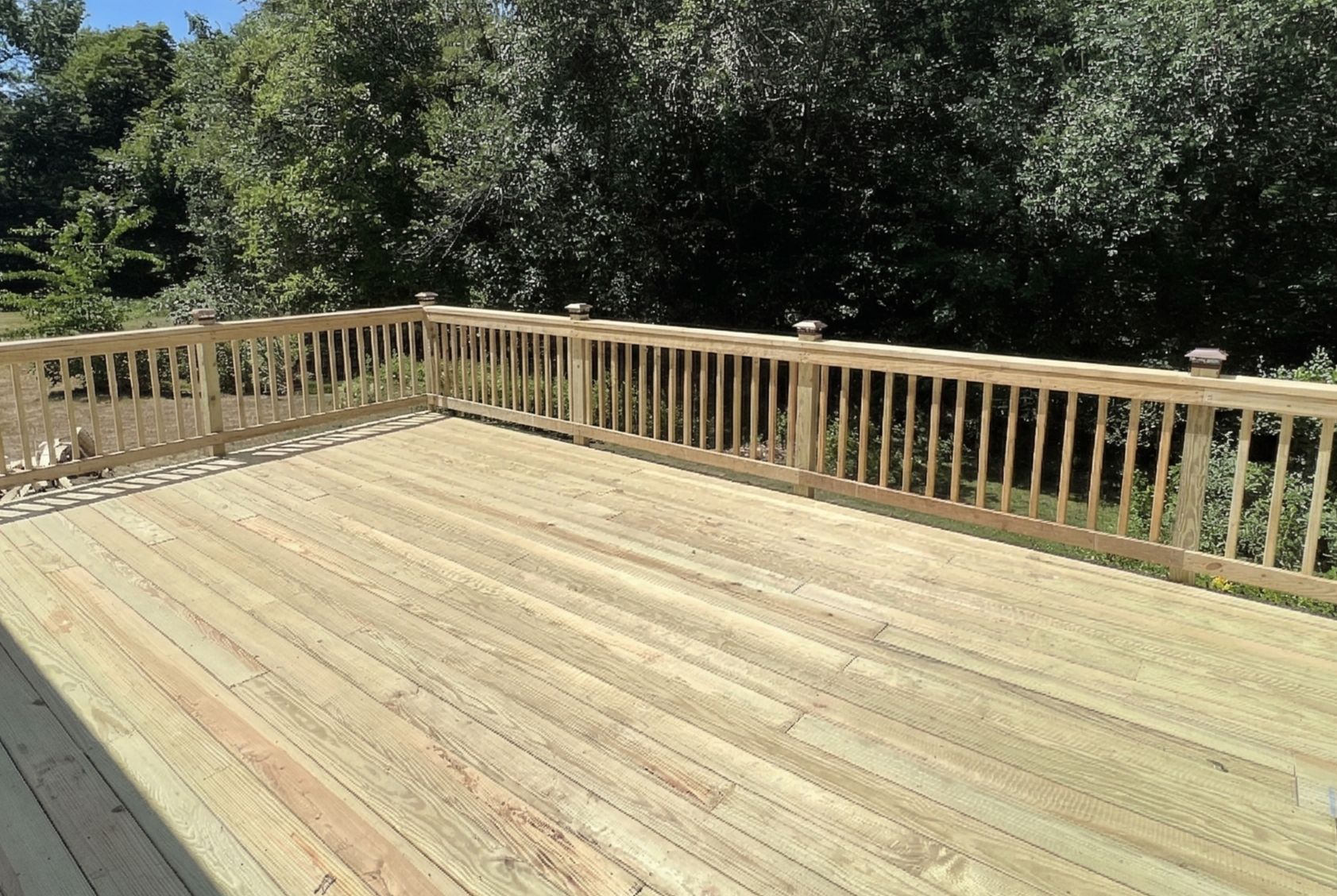 Wooden deck with a railing and trees in the background.