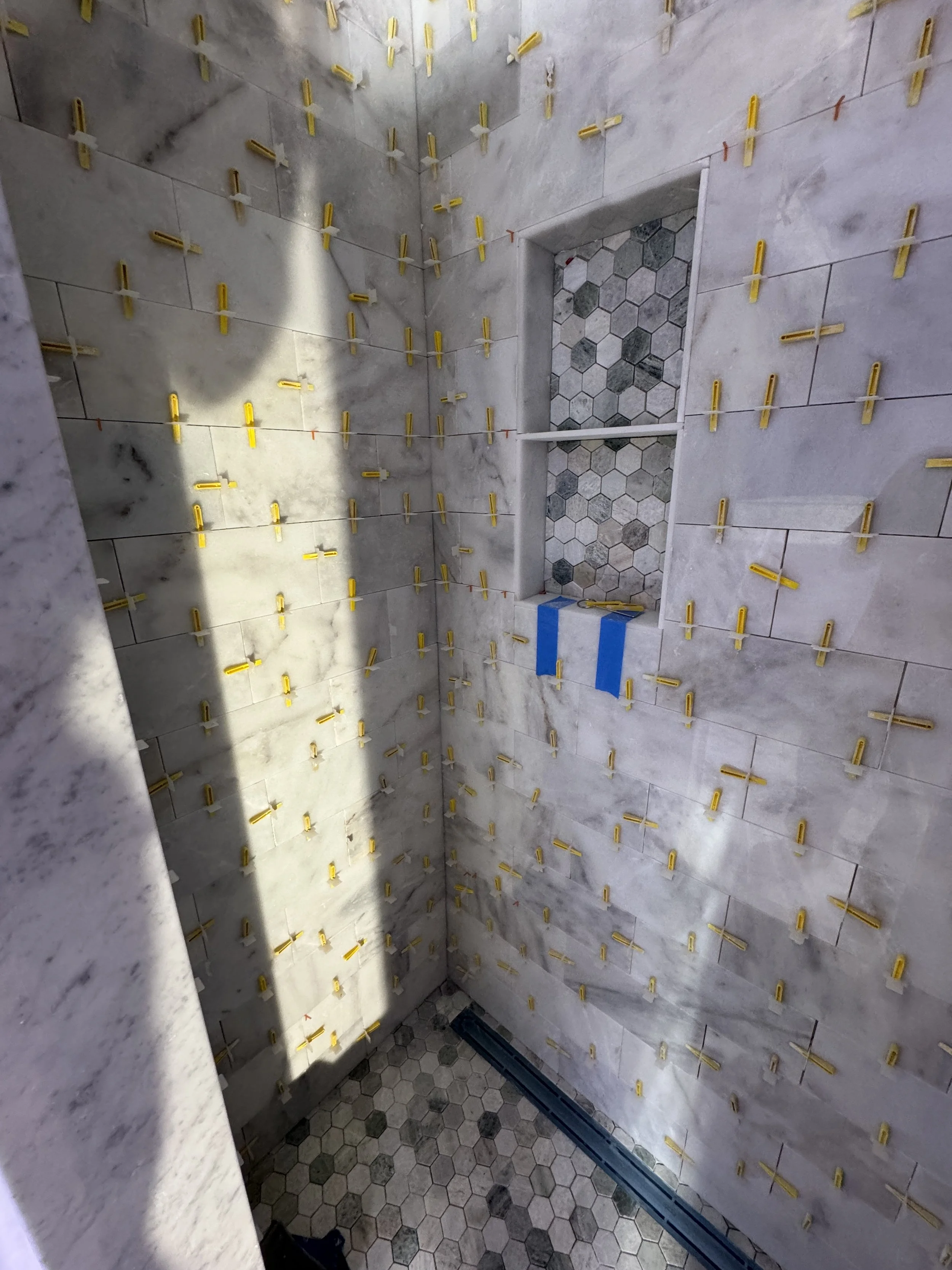 Bathroom shower with tiles and yellow tile spacers, some taped areas, and hexagonal accent tiles in the niche.