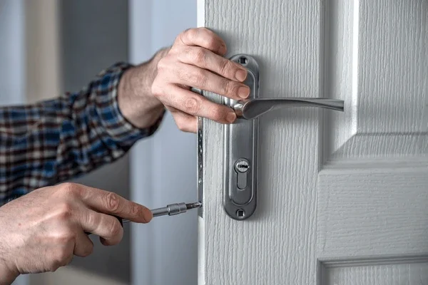 Person installing or repairing a door lock with a screwdriver.
