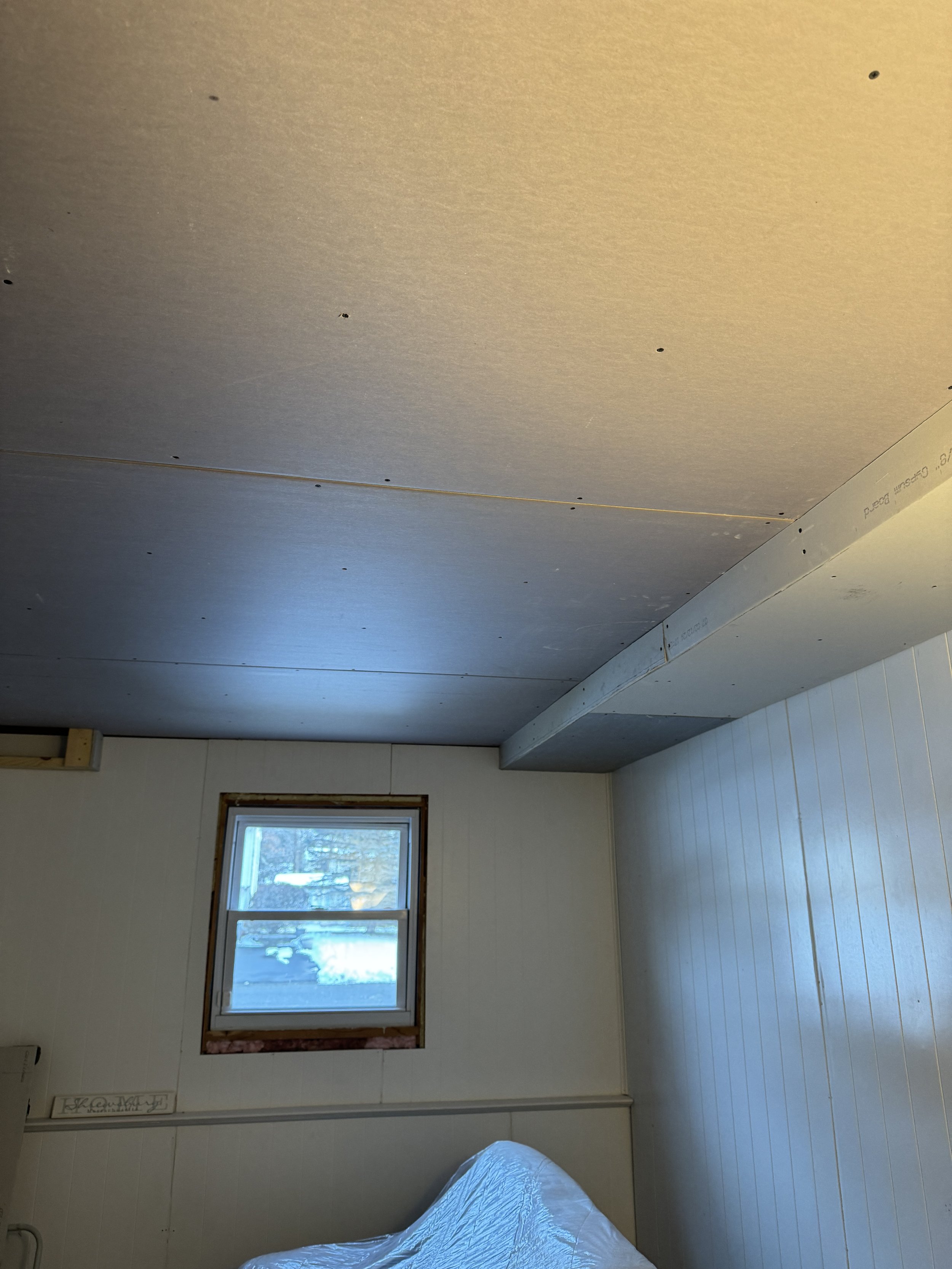 A room under construction with a partially installed ceiling, a window showing an outdoor view, and unfinished walls.