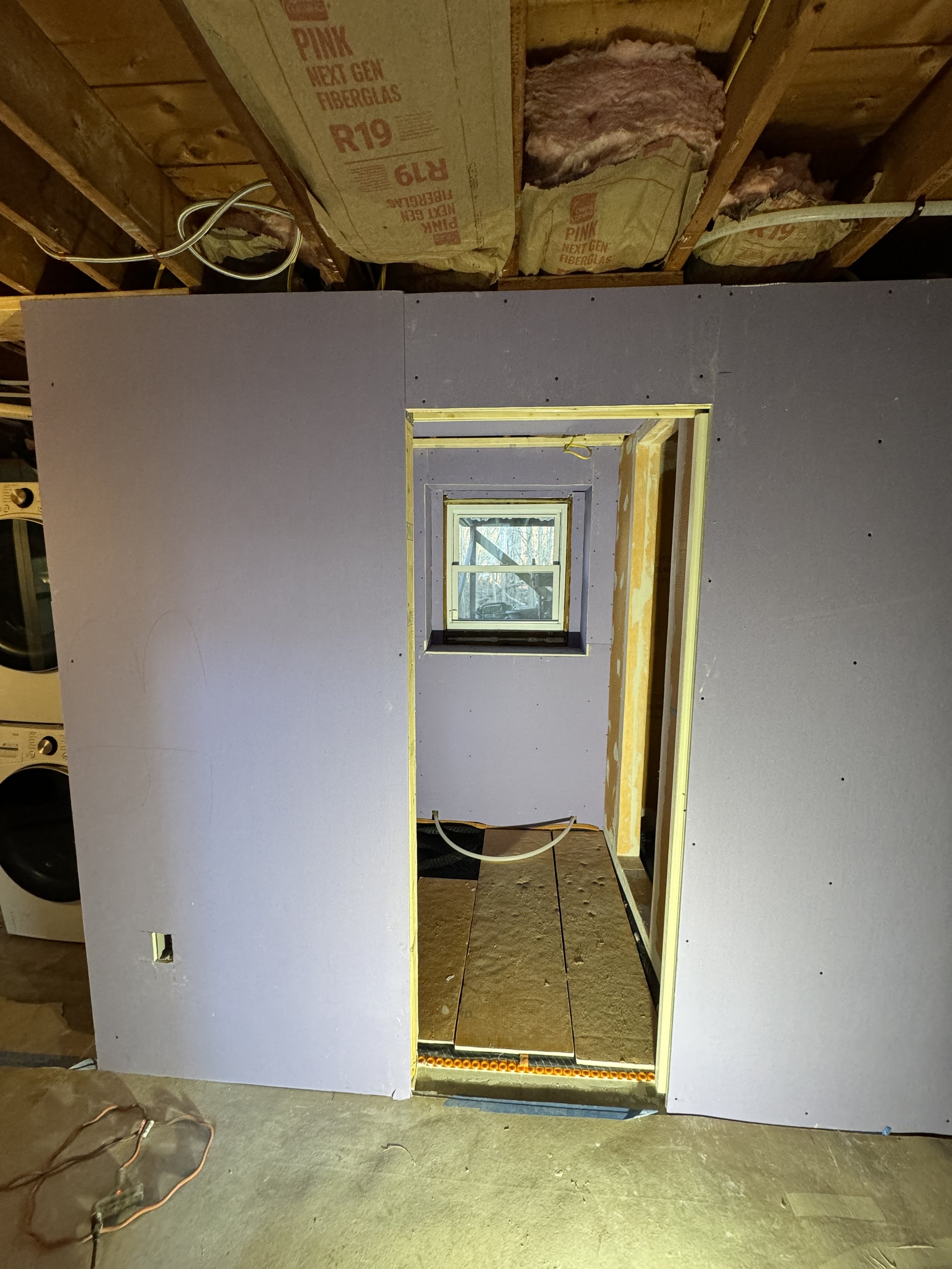 Construction of an interior room with drywall partially installed, a small window, and unfinished flooring in a home renovation project.