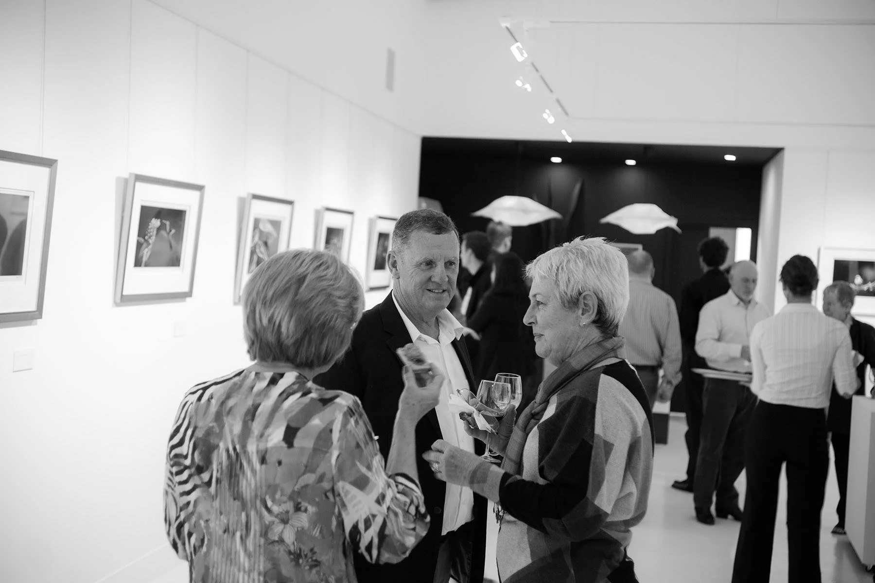 People attending an art gallery event, engaging in conversations and viewing artwork.