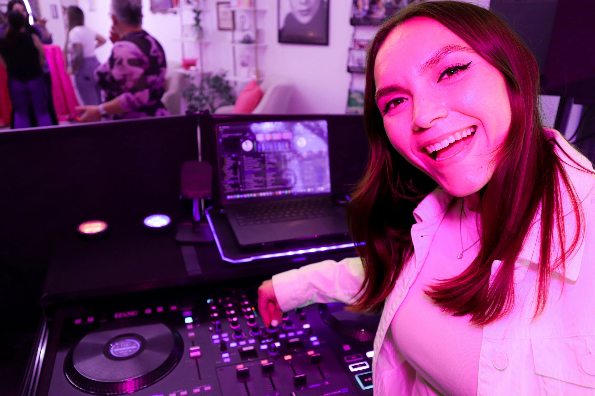 Young woman smiling while DJing at a party with colorful lighting.