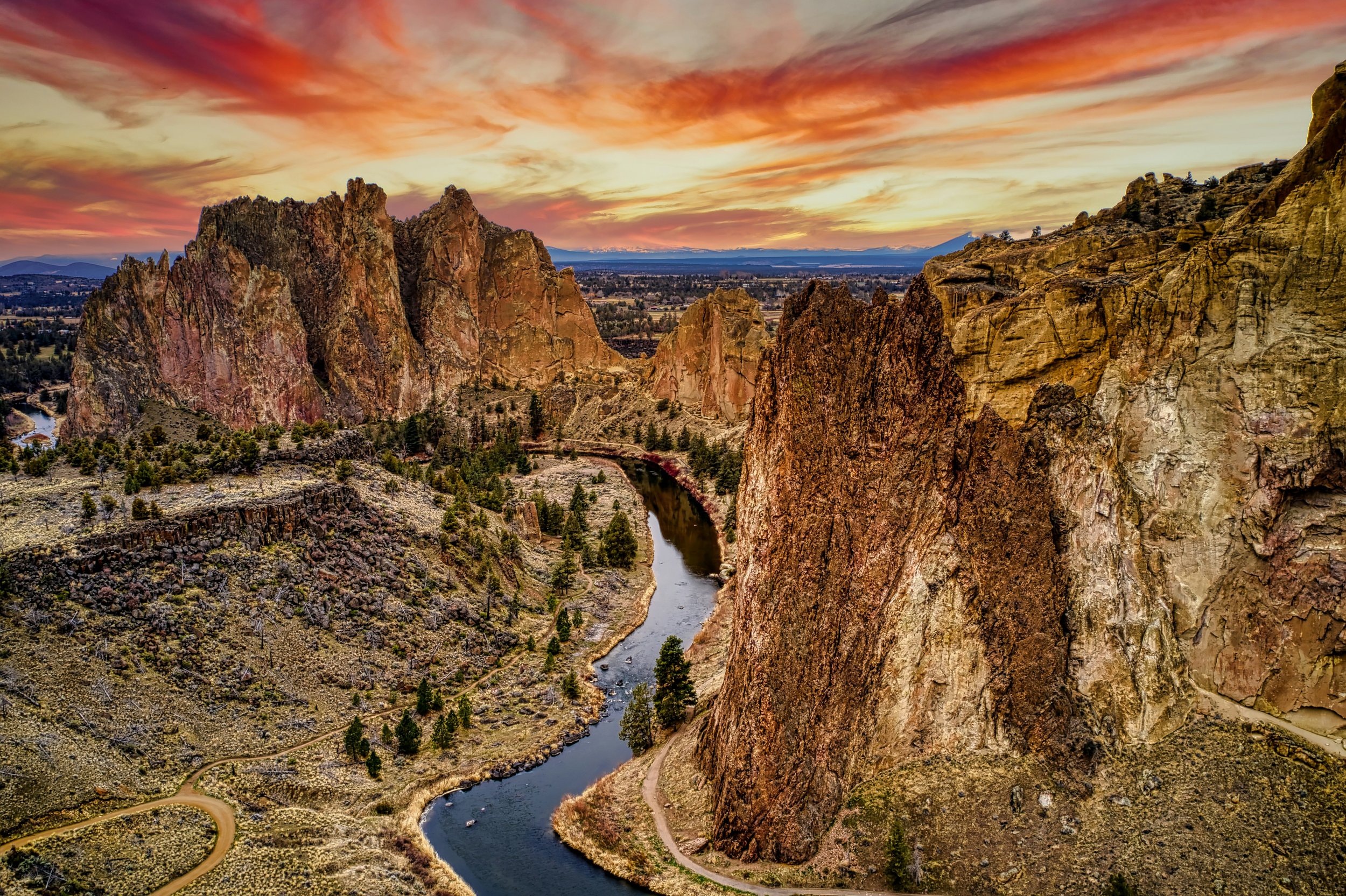 Sunset over jagged mountain peaks and a winding river in a desert landscape.