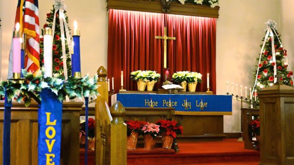 church decorated for Christmas with flowers, poinsettias, candles, and holiday banners.