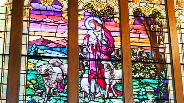 Colorful stained glass window depicting a shepherd with a lamb in a pastoral landscape.