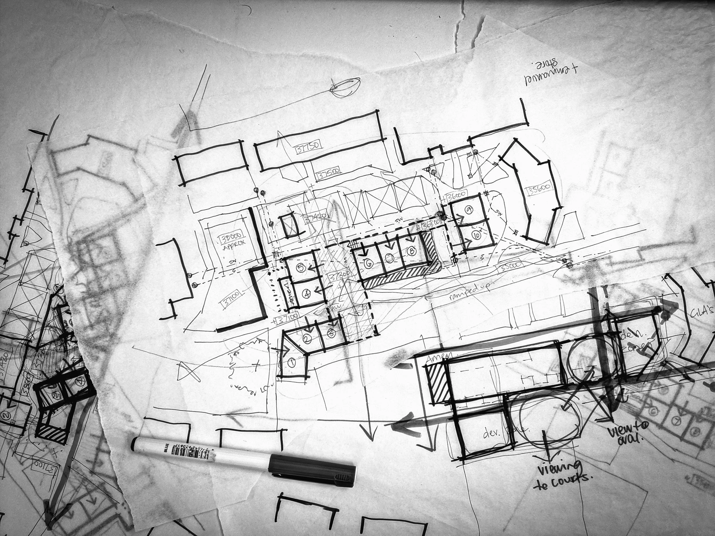 Architectural blueprint sketches on paper, with various notes and drawings, including a pen at the bottom.