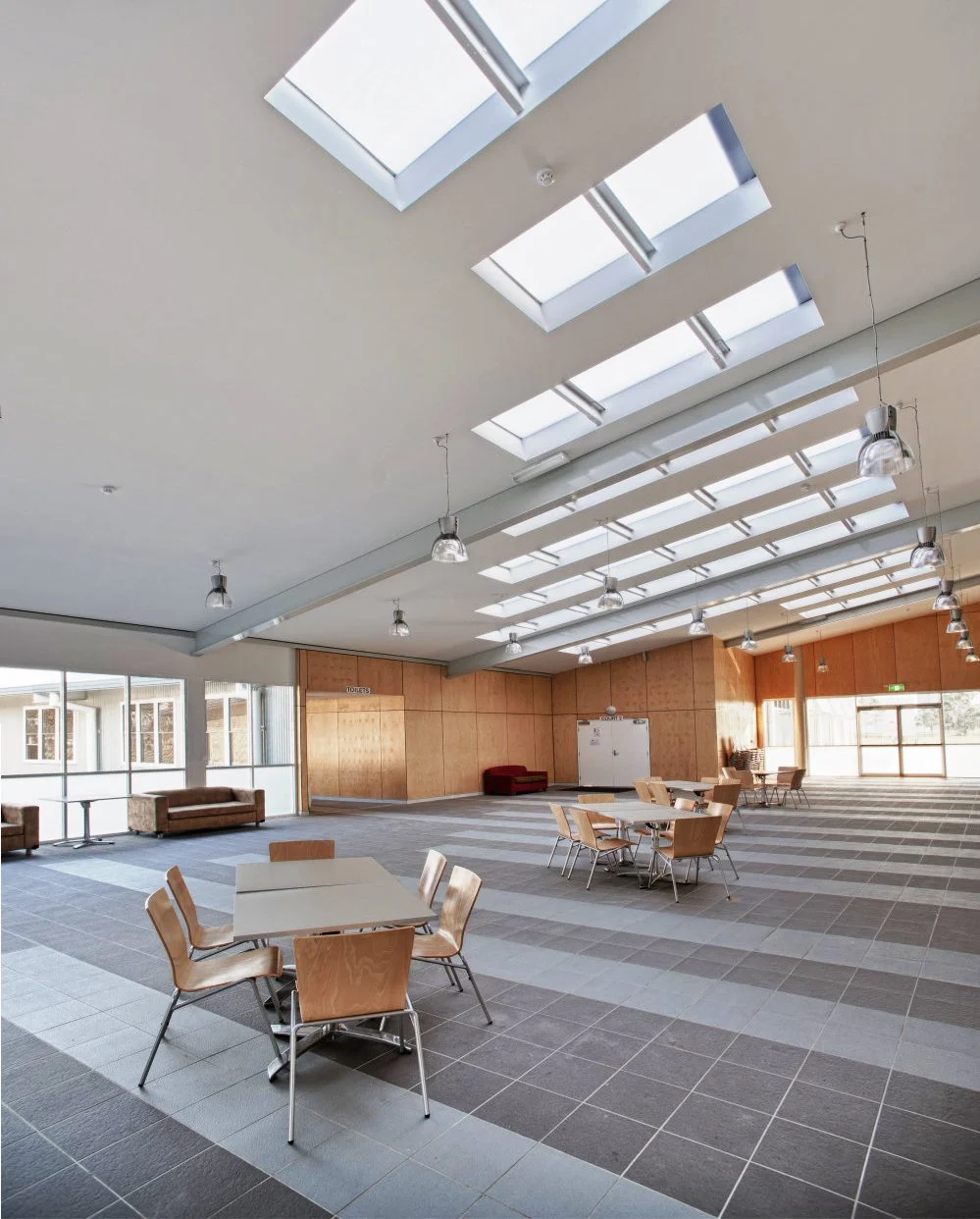 Empty indoor room with tables, chairs, skylights, and wooden wall panels.