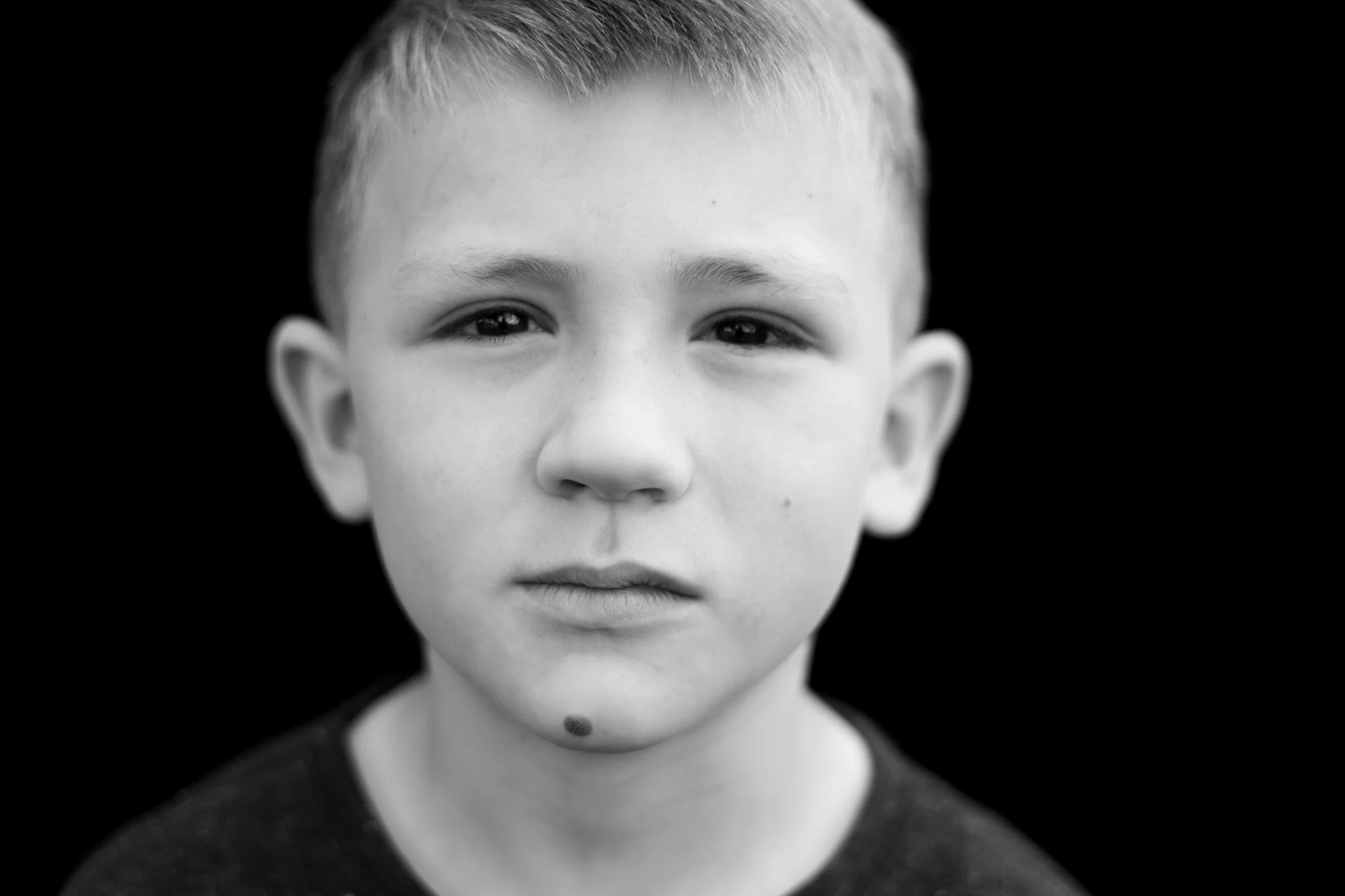 Close-up black-and-white portrait of a young boy with short hair, looking directly at the camera with a neutral expression.